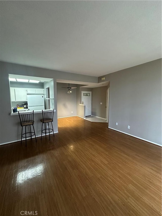 unfurnished living room featuring wood finished floors, baseboards, and ceiling fan