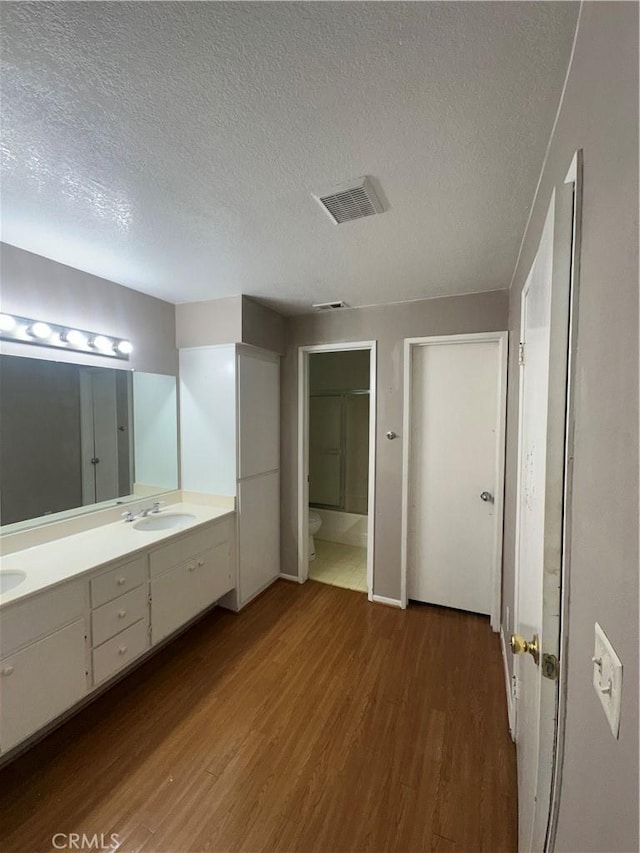 full bath featuring wood finished floors, visible vents, double vanity, a sink, and toilet