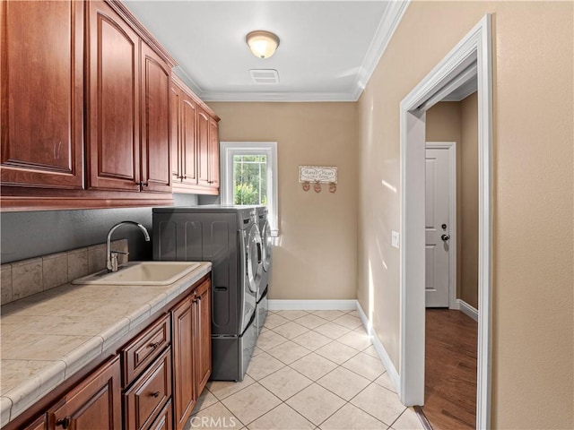 laundry room featuring washing machine and clothes dryer, baseboards, ornamental molding, cabinet space, and a sink