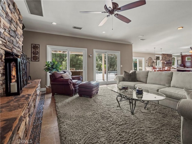 living room featuring visible vents, a stone fireplace, crown molding, and ceiling fan