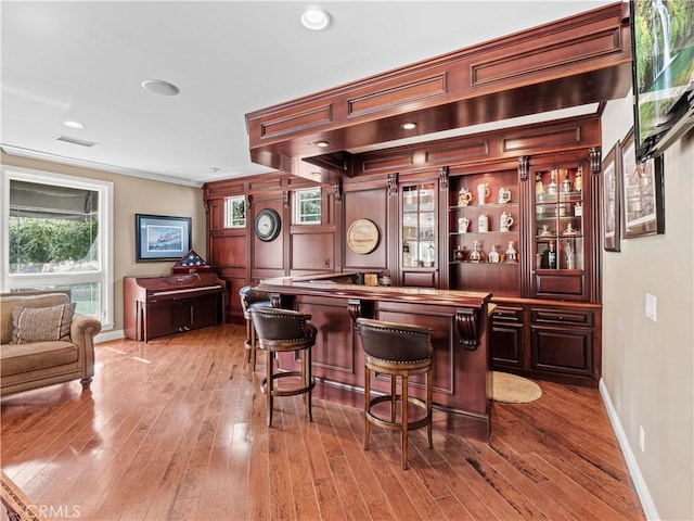 bar featuring visible vents, crown molding, baseboards, indoor bar, and wood-type flooring