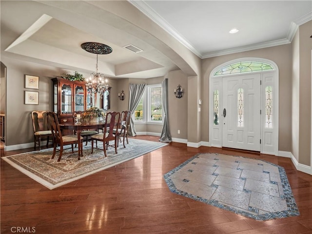 foyer entrance featuring wood finished floors, visible vents, baseboards, a tray ceiling, and arched walkways