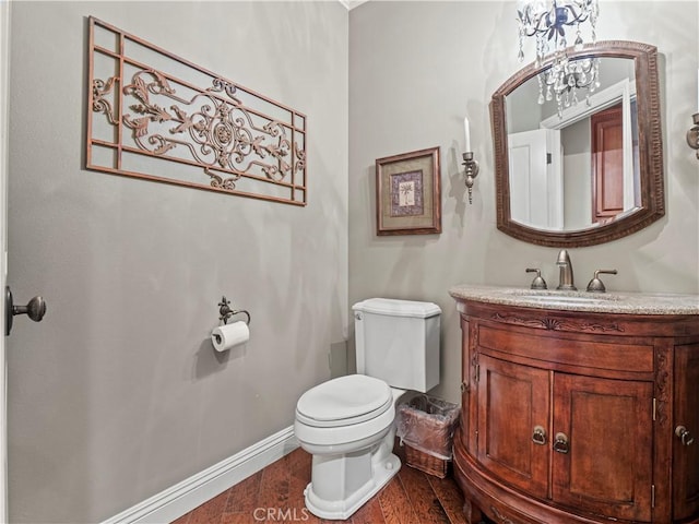 half bath featuring vanity, toilet, wood finished floors, and baseboards