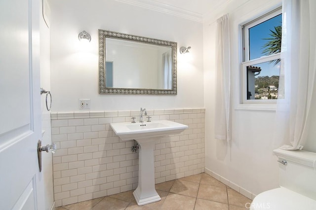 half bathroom featuring toilet, ornamental molding, wainscoting, tile patterned floors, and tile walls