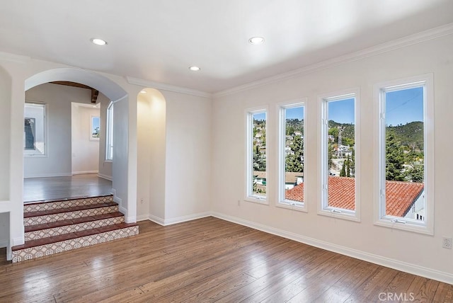 spare room with arched walkways, baseboards, a wealth of natural light, and hardwood / wood-style flooring