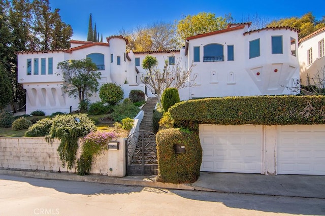 mediterranean / spanish-style home with stucco siding, a fenced front yard, concrete driveway, an attached garage, and a tiled roof