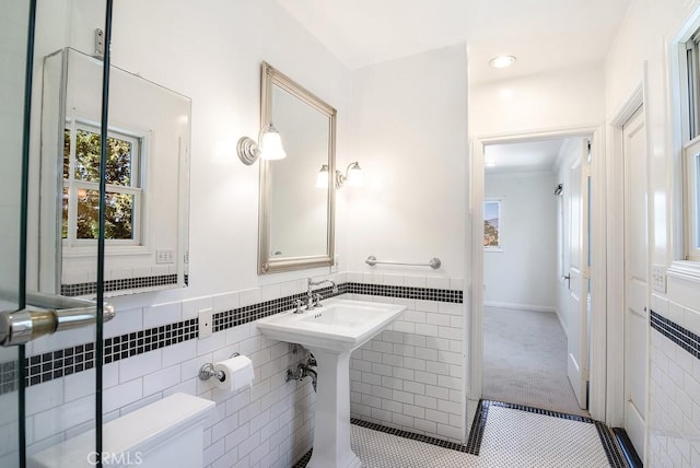 half bath with tile patterned flooring, tile walls, toilet, and a wainscoted wall