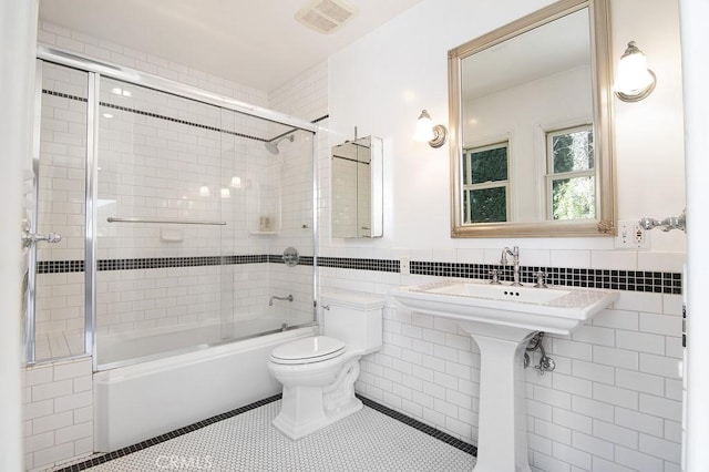 bathroom with visible vents, shower / bath combination with glass door, tile patterned flooring, tile walls, and toilet