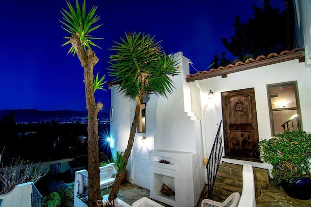 exterior entry at twilight featuring stucco siding, a fireplace, and a tile roof