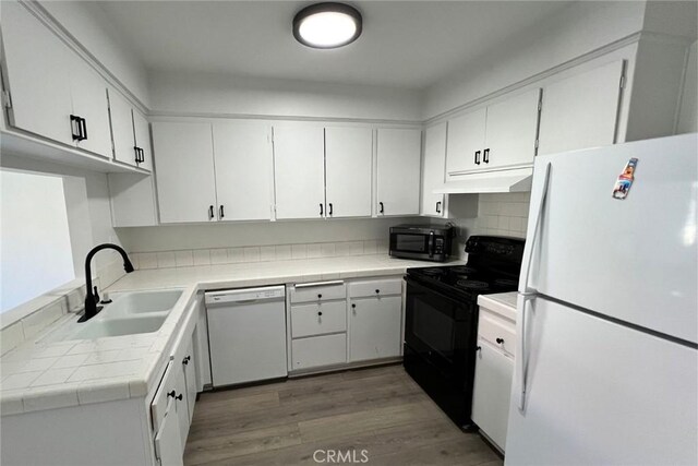 kitchen featuring tile counters, under cabinet range hood, light wood-style flooring, black appliances, and a sink