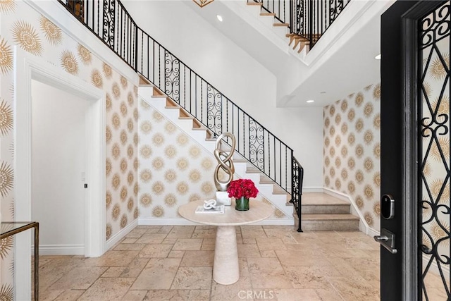 foyer with stone tile flooring, wallpapered walls, a high ceiling, and baseboards