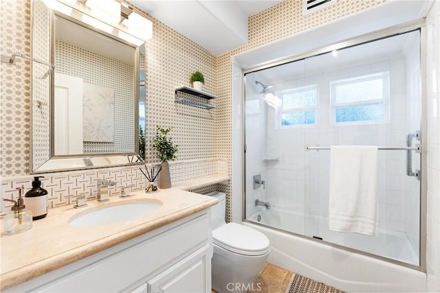 bathroom featuring wallpapered walls, toilet, decorative backsplash, combined bath / shower with glass door, and vanity