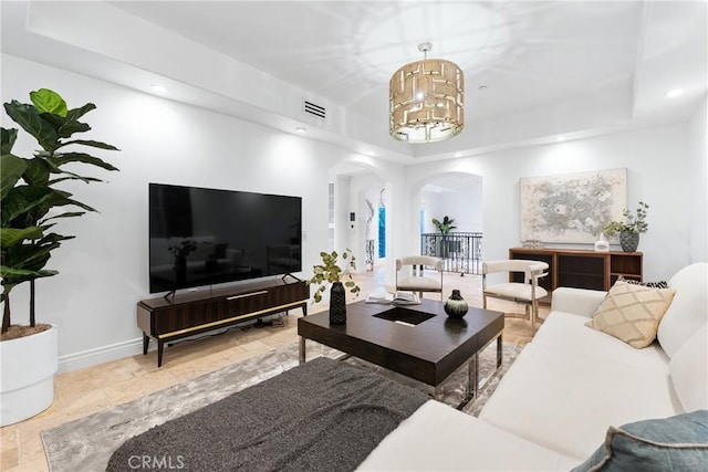 living area featuring visible vents, baseboards, a chandelier, a tray ceiling, and arched walkways
