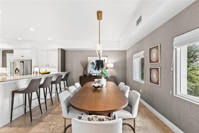 dining space with stone tile floors, a healthy amount of sunlight, wallpapered walls, and baseboards
