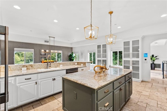 kitchen featuring a sink, arched walkways, stone tile flooring, and white cabinets