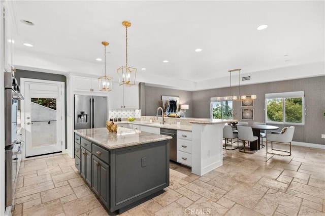 kitchen featuring stone tile floors, a peninsula, a sink, stainless steel appliances, and white cabinetry