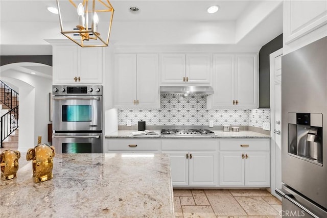 kitchen with under cabinet range hood, arched walkways, appliances with stainless steel finishes, and white cabinetry