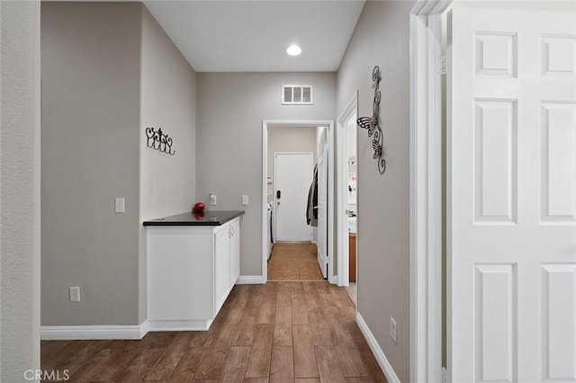 corridor featuring visible vents, baseboards, and wood finished floors