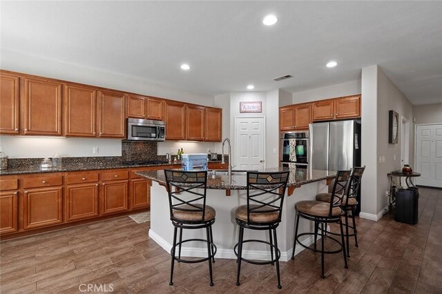 kitchen with stainless steel appliances, an island with sink, and brown cabinetry