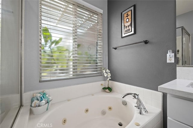 bathroom featuring a healthy amount of sunlight, a jetted tub, vanity, and a textured wall