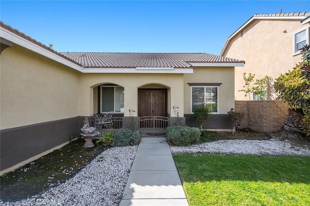 property entrance with fence, a tiled roof, covered porch, a lawn, and stucco siding