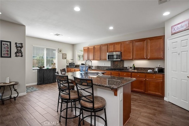 kitchen featuring stainless steel microwave, brown cabinetry, visible vents, and a sink