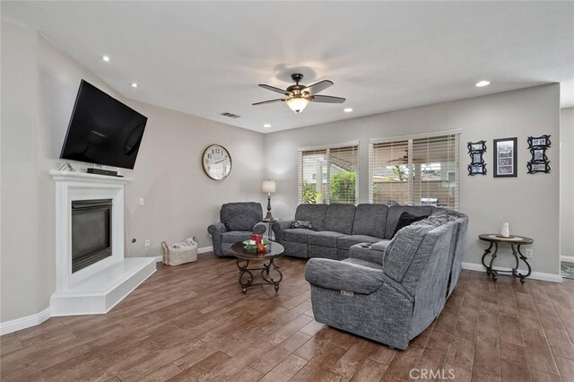 living room with wood finished floors, visible vents, baseboards, recessed lighting, and a glass covered fireplace