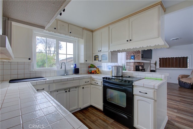 kitchen with dark wood-type flooring, black range with electric stovetop, a sink, a peninsula, and tile counters