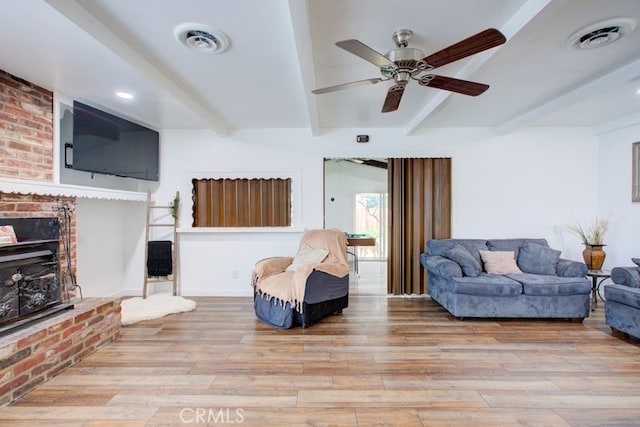 living room with beamed ceiling, a fireplace, visible vents, and light wood finished floors