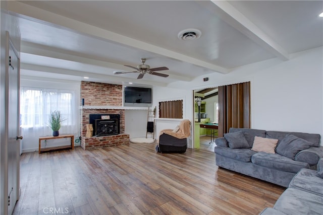 living room with wood finished floors, visible vents, beam ceiling, a fireplace, and ceiling fan