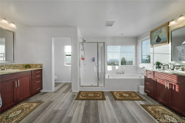 full bath featuring toilet, a stall shower, a sink, wood finished floors, and a bath