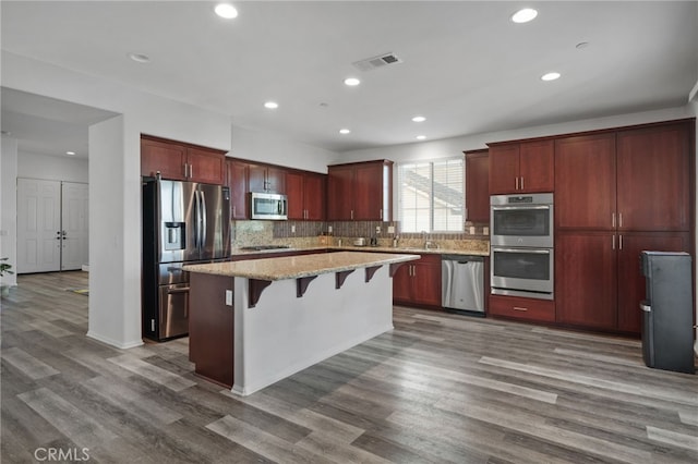 kitchen featuring reddish brown cabinets, a kitchen island, appliances with stainless steel finishes, and dark wood-style flooring