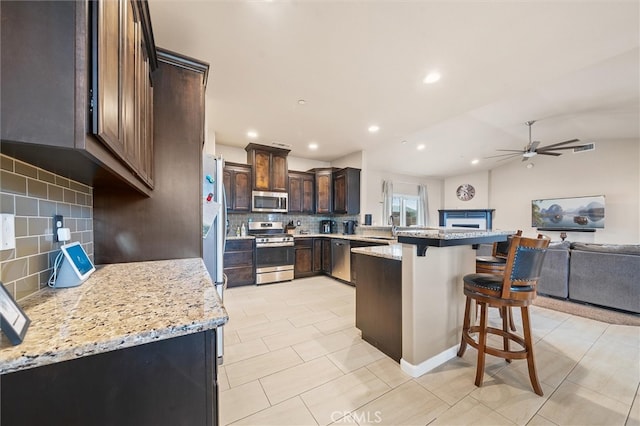 kitchen with a kitchen bar, a sink, open floor plan, a peninsula, and appliances with stainless steel finishes