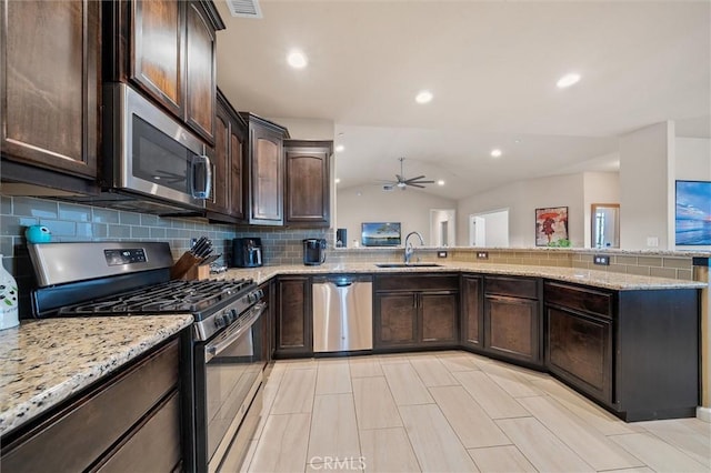 kitchen with light stone counters, a sink, stainless steel appliances, dark brown cabinetry, and vaulted ceiling