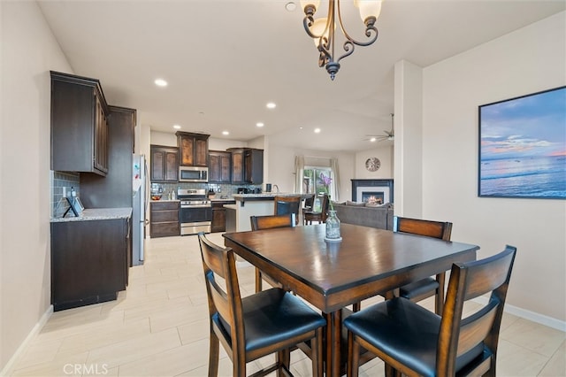 dining space featuring recessed lighting, baseboards, a lit fireplace, and ceiling fan with notable chandelier