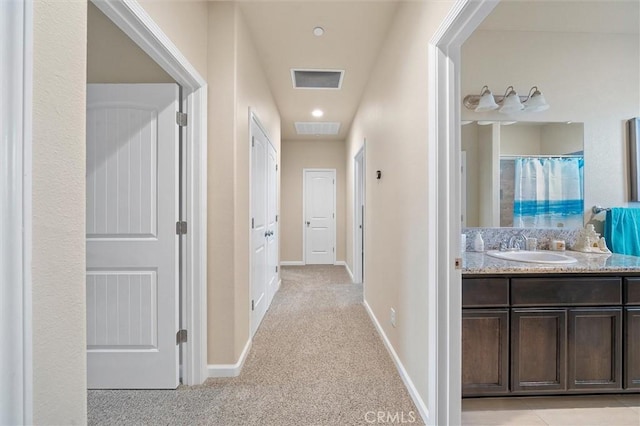 hallway with light carpet, visible vents, baseboards, and a sink