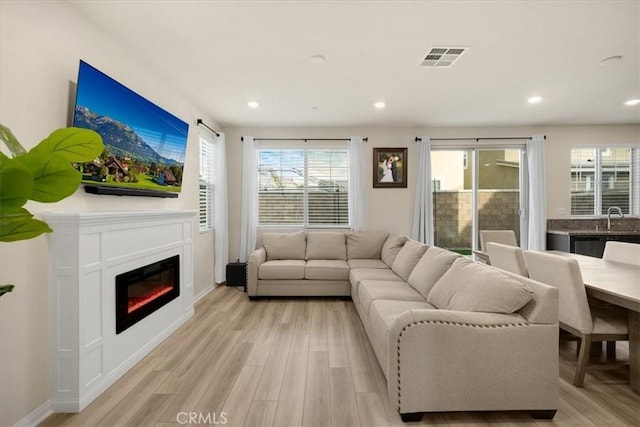 living area with a glass covered fireplace, visible vents, light wood-style flooring, and recessed lighting