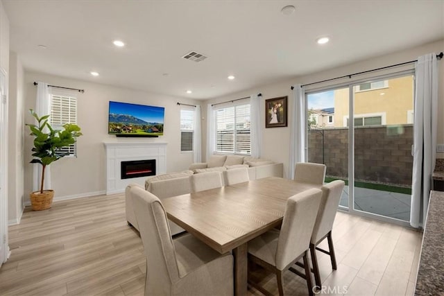 dining area featuring light wood-type flooring, visible vents, a warm lit fireplace, and recessed lighting