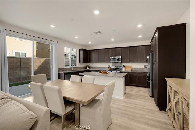 kitchen featuring visible vents, a sink, a kitchen island, dark brown cabinetry, and appliances with stainless steel finishes