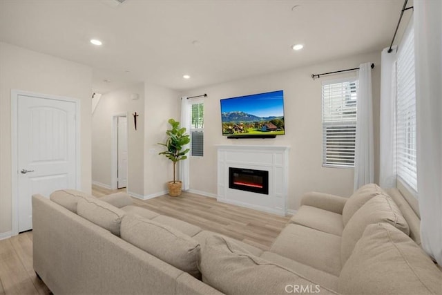 living area with a glass covered fireplace, recessed lighting, light wood-type flooring, and baseboards