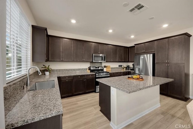 kitchen featuring visible vents, dark brown cabinets, light wood-type flooring, appliances with stainless steel finishes, and a sink