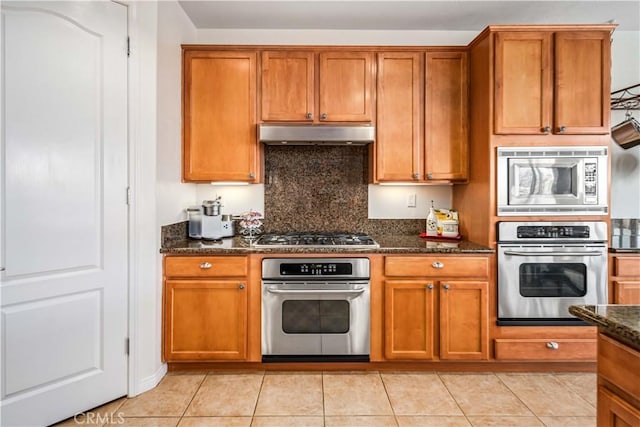 kitchen featuring range hood, light tile patterned flooring, brown cabinetry, and stainless steel appliances