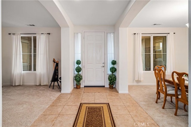 entrance foyer with light tile patterned floors, arched walkways, and light carpet