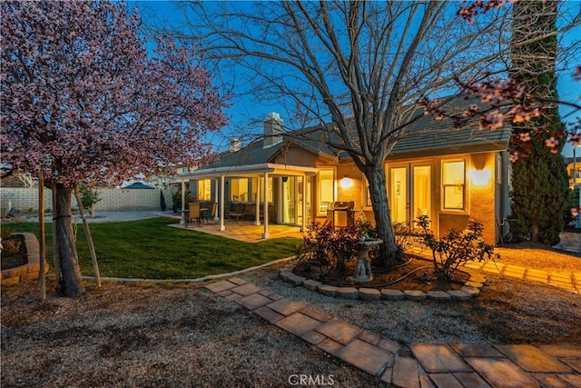 back of house featuring stucco siding, a lawn, a patio, fence, and a chimney