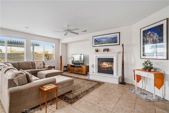 living area featuring visible vents, a ceiling fan, a glass covered fireplace, light tile patterned flooring, and baseboards