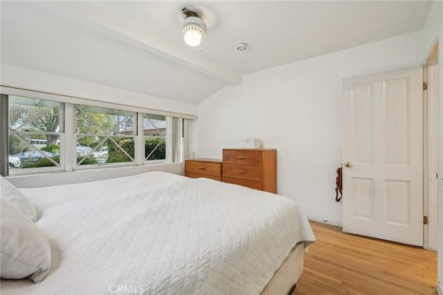 bedroom with light wood-type flooring and vaulted ceiling with beams