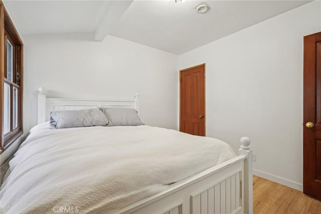 bedroom with baseboards, light wood-style flooring, and vaulted ceiling with beams