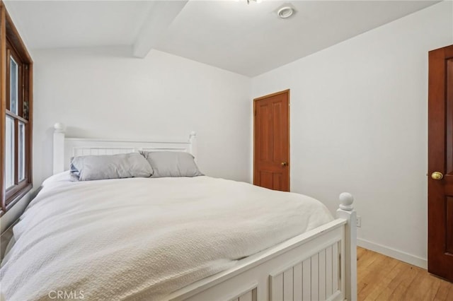 bedroom featuring baseboards, vaulted ceiling with beams, and light wood-style flooring