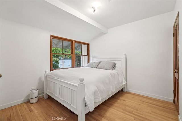 bedroom with light wood-style flooring, vaulted ceiling with beams, and baseboards