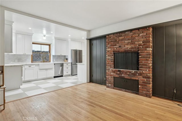 kitchen with light wood-style flooring, stainless steel appliances, white cabinets, light countertops, and decorative backsplash